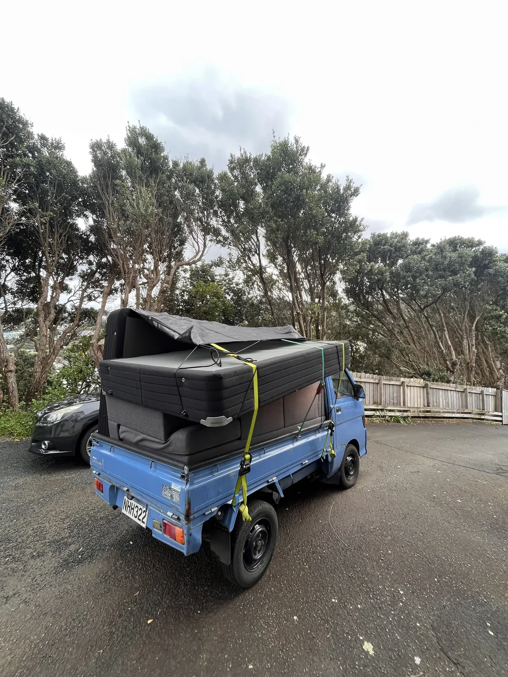Tiny Truck carrying a large dark couch strapped and tarped for a furniture move
