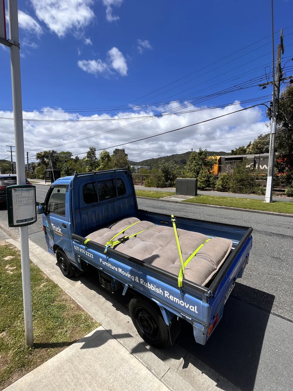 Tiny Truck carrying a large seat cushion strapped flat on the deck for a furniture move