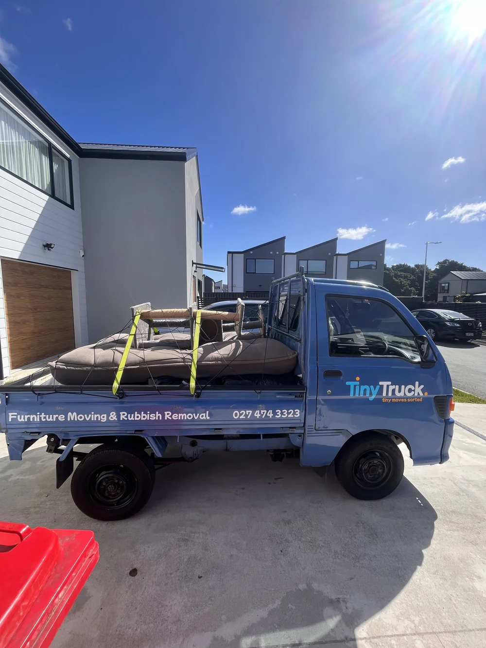 Tiny Truck loaded with an old couch and cushions outside new townhouses for removal