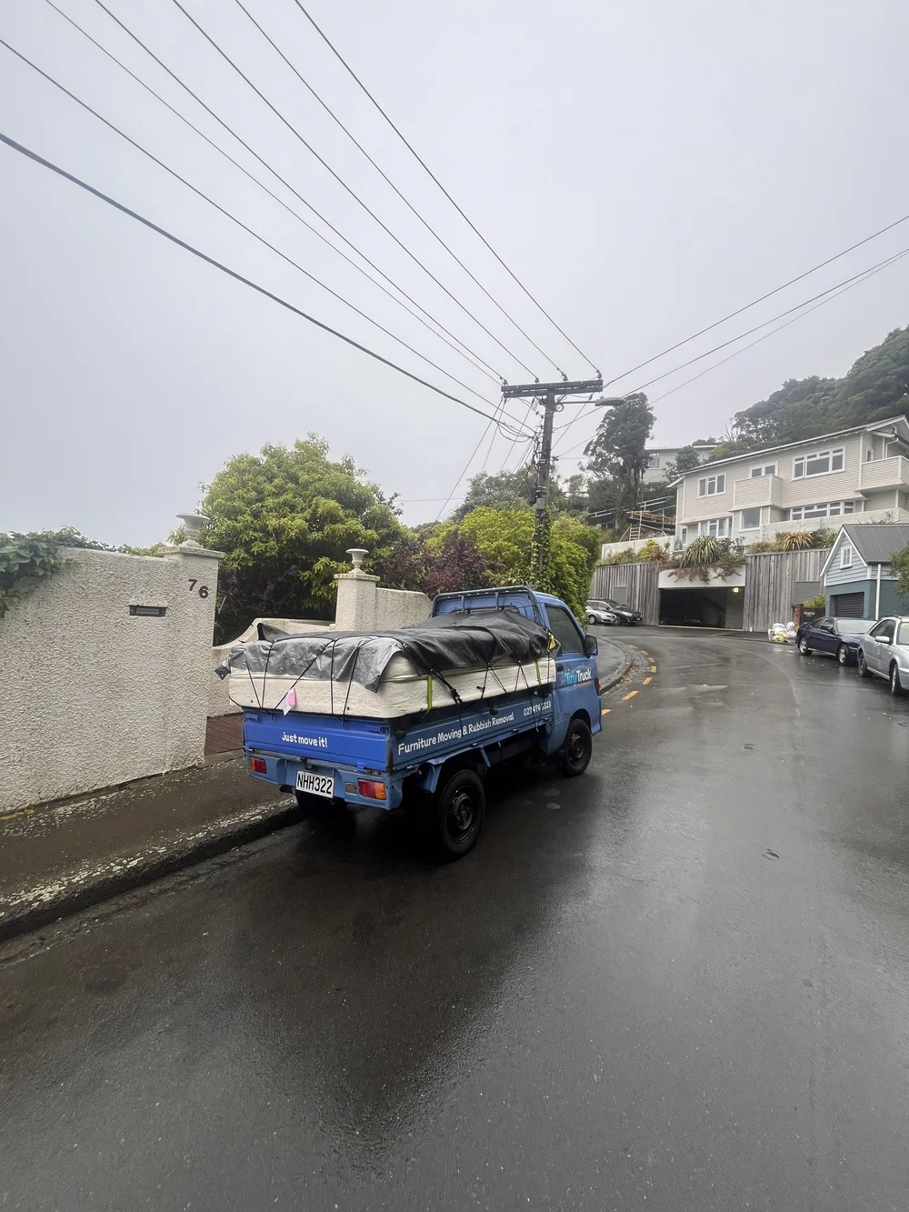 Tiny Truck on a wet hillside street with mattresses tarped and netted for a move