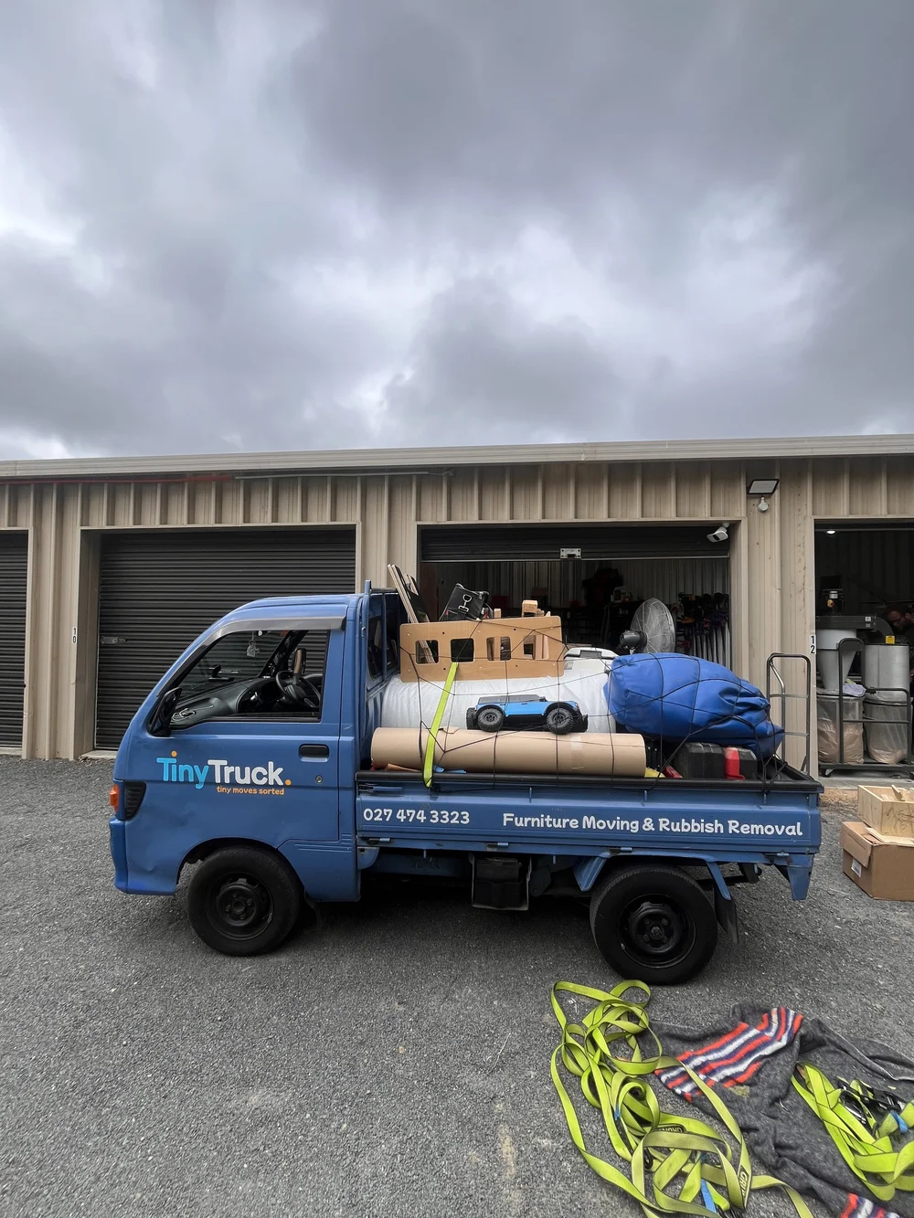 Tiny Truck loaded with workshop items, a fan and bags outside storage units for a move