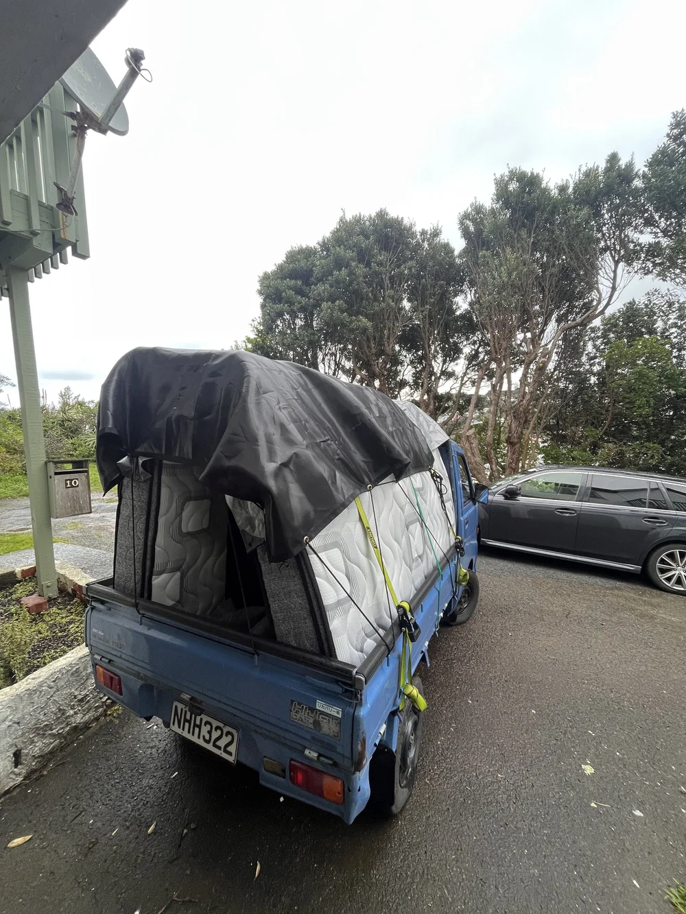 Tiny Truck loaded with mattresses and a bed base under a tarp, ready to move