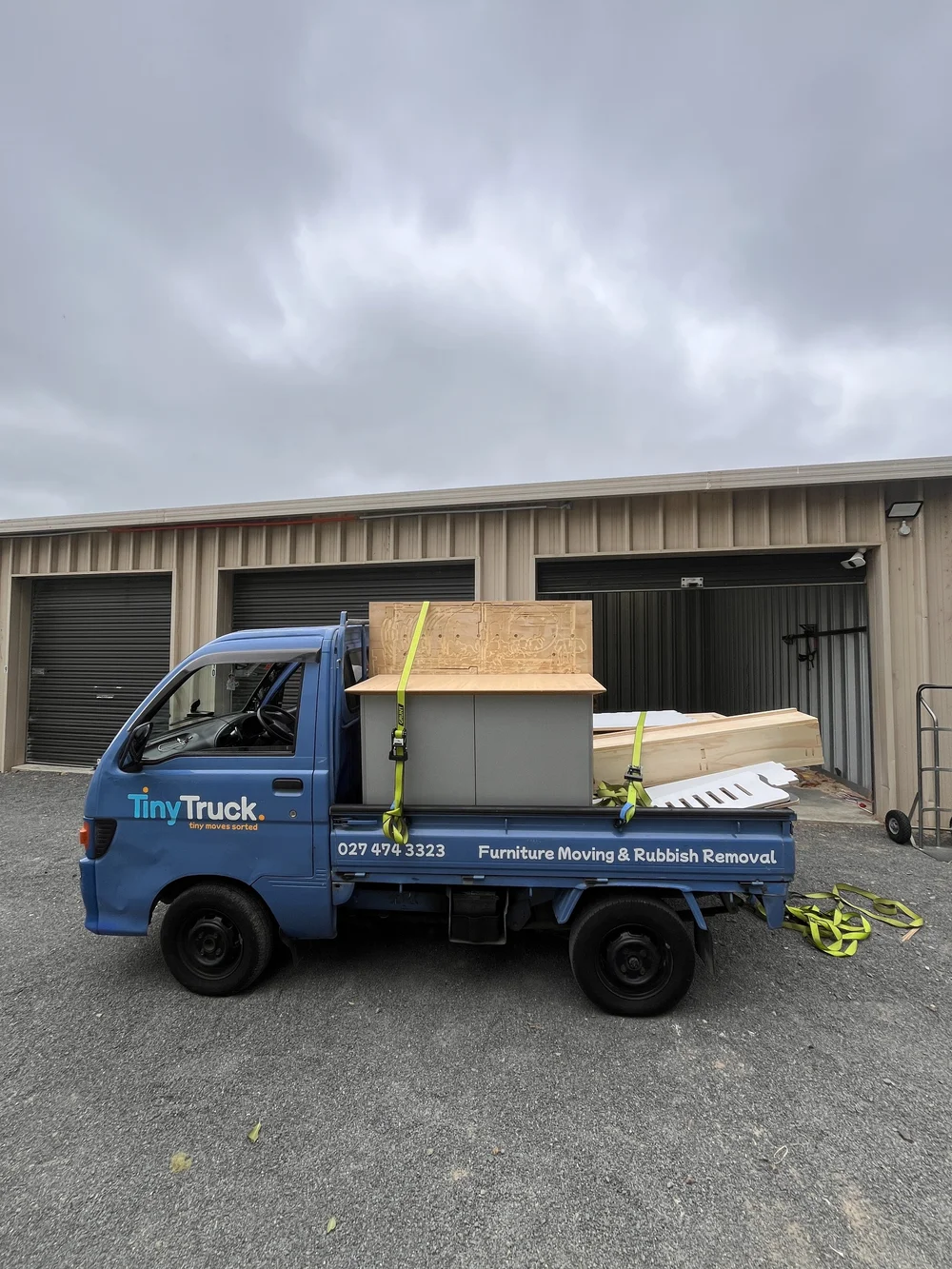 Tiny Truck carrying a grey cabinet and plywood sheets outside storage units