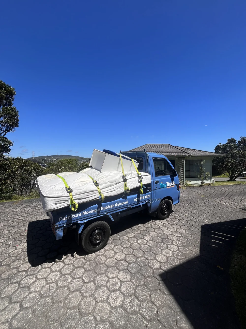 Tiny Truck with old mattresses and a white panel strapped down for a rubbish removal run