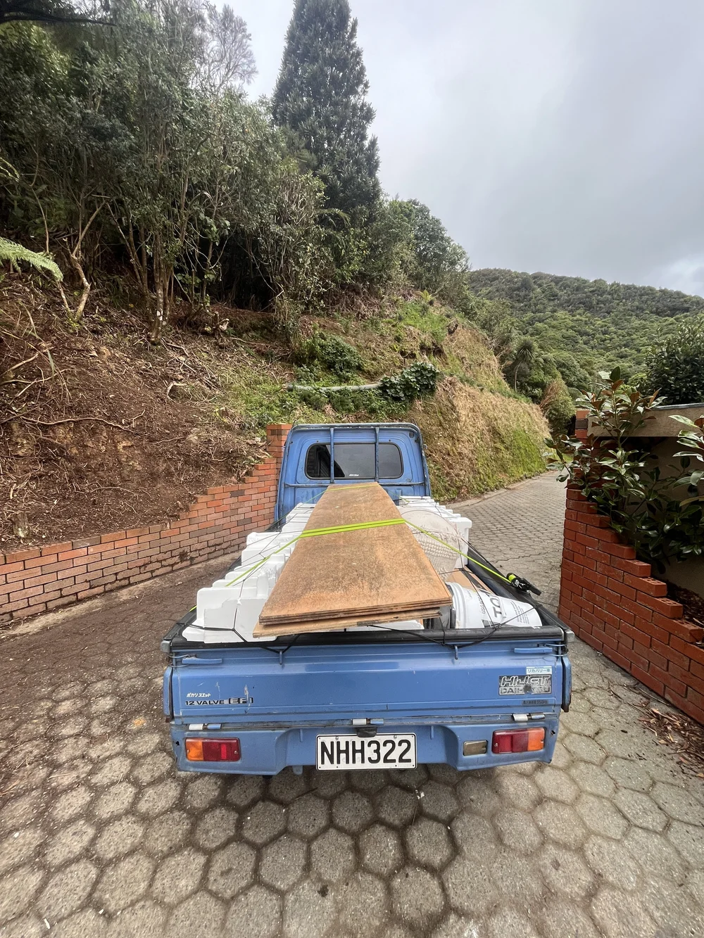 Tiny Truck on a brick driveway carrying plywood sheets and white plastic tubs for removal