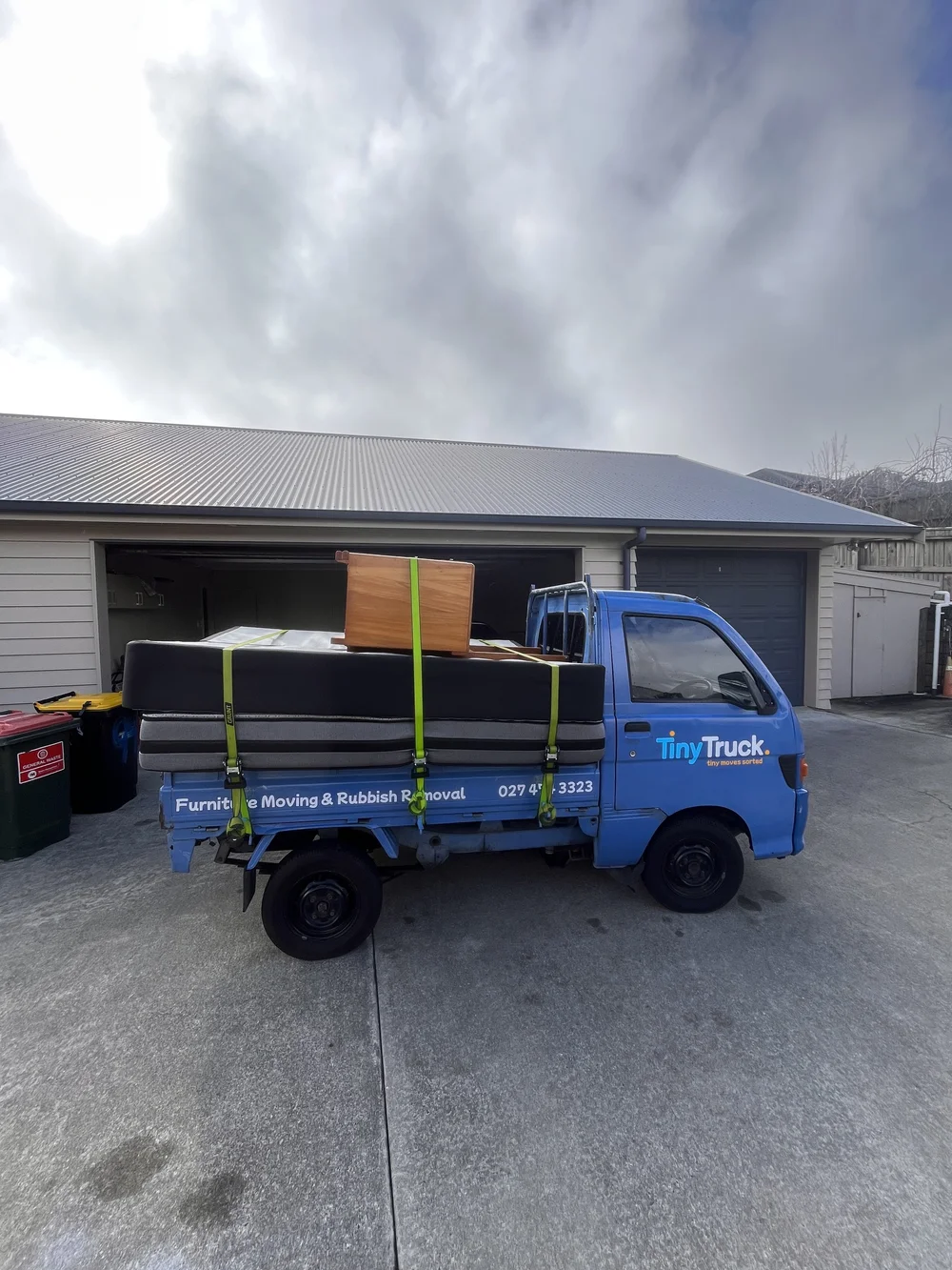 Tiny Truck outside a garage with a mattress and wooden drawers strapped down for a move