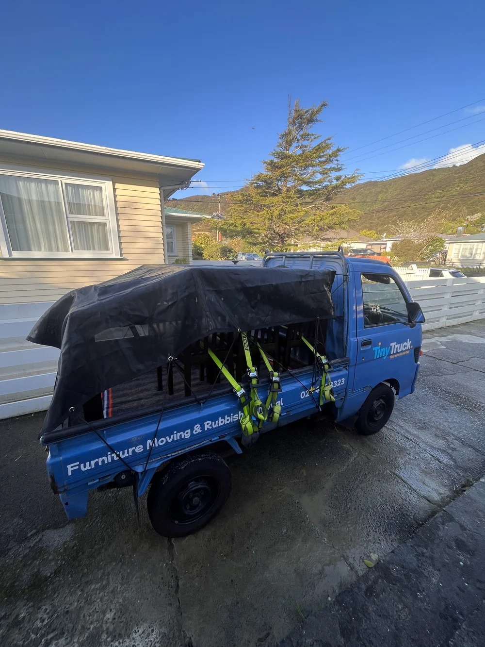 Tiny Truck with dining chairs and furniture under a tarp, strapped down for a house move