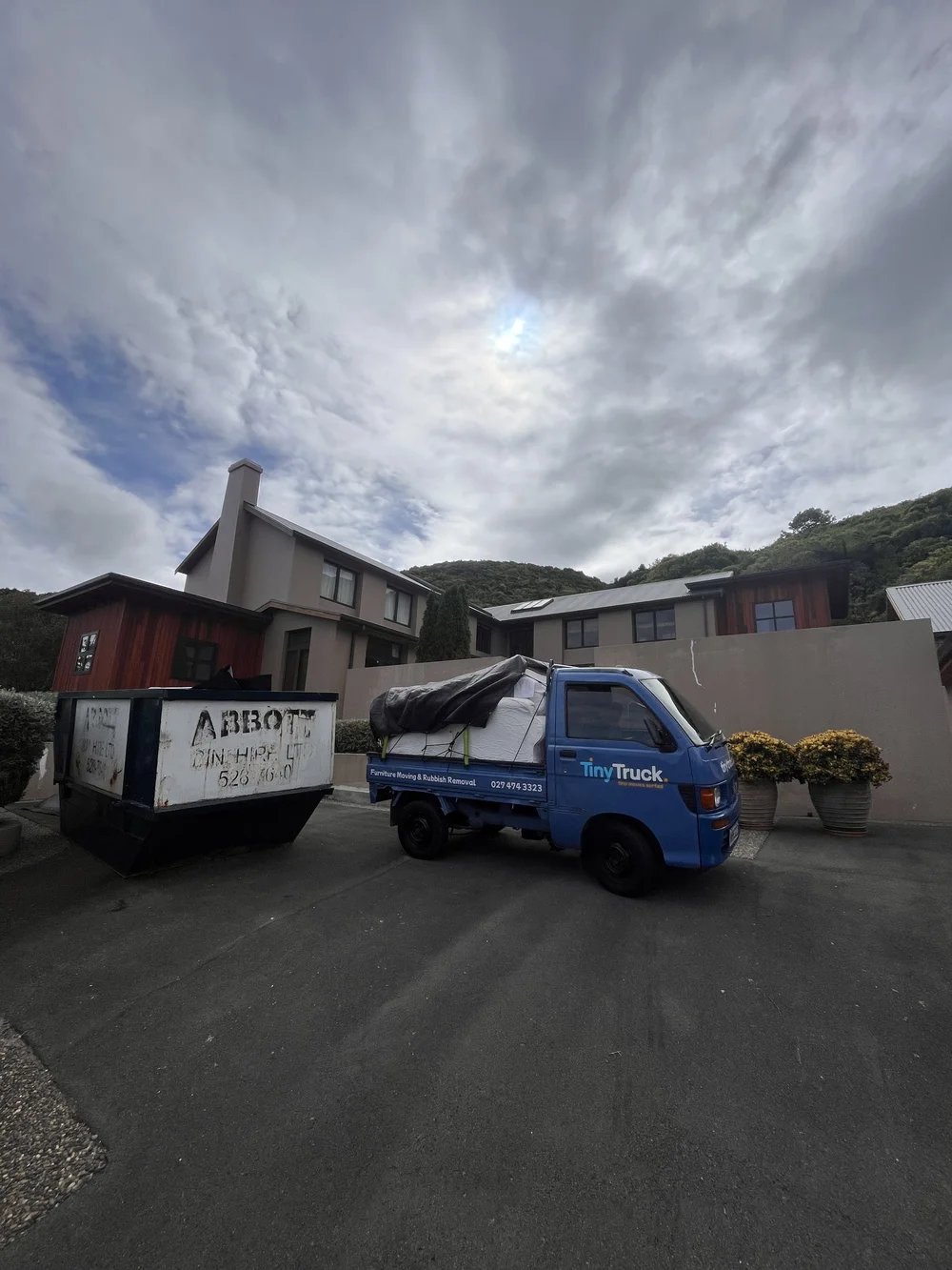 Tiny Truck with a tarped load parked beside a skip bin during a house clear-out